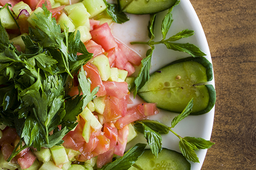Cucumbers, tomatoes, and mint beautifully arranged on a plate.