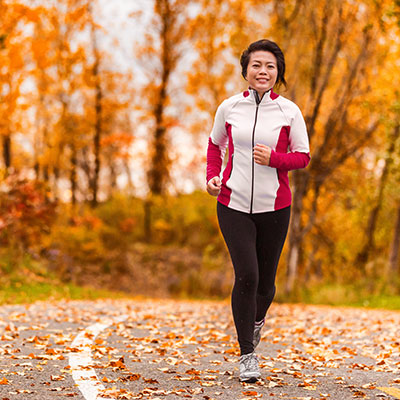 An active woman running in a park with autumn leaves.