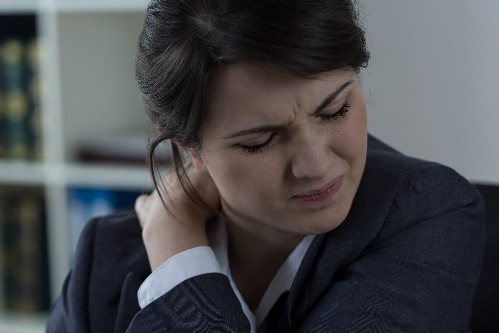 A business woman holds her neck and appears to be in pain.
