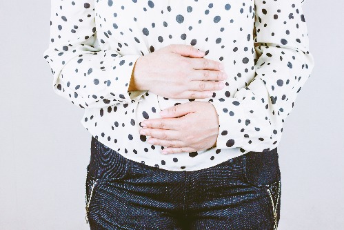 A woman with a round stomach holding her middle, suggesting that she feels unwell.