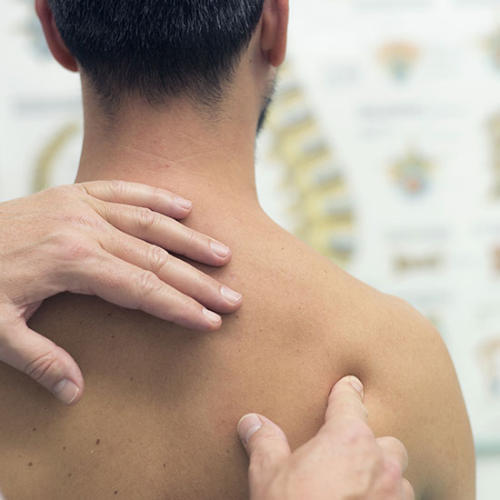 A doctor examines a man's shoulder with an illustration of the spine in the background.